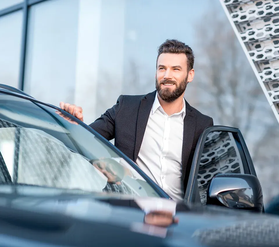 Gewerbetreibender Mann im Anzug steht vor seinem Firmenleasing-Fahrzeug und freut sich aufgrund der guten Fahrzeugleasing- und Servicekonditionen 