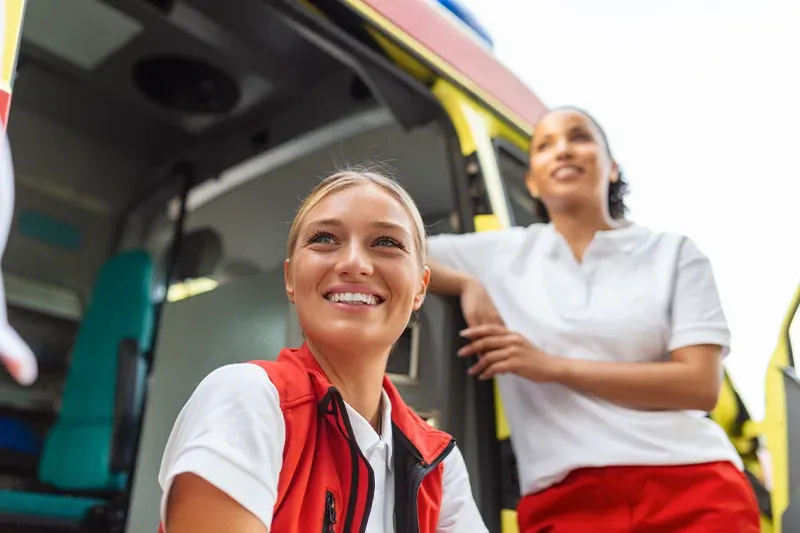Rettungssanit&auml;ter und Rettungssanit&auml;terin l&auml;cheln vor Notarztfahrzeug und Rettungswagen