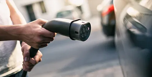 Person h&auml;lt Ladestecker f&uuml;r E-Fahrzeug oder Plug-In-Hybrid-Fahrzeug