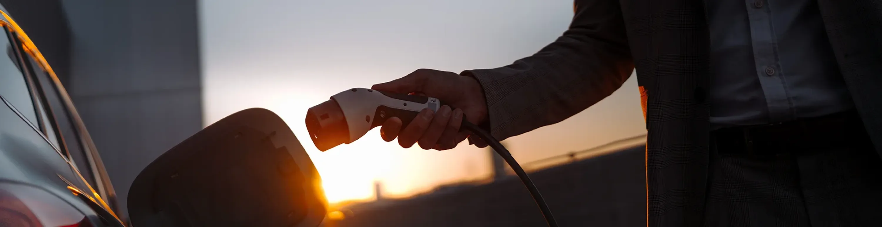 Mann in Anzug l&auml;dt sein Elektrofahrzeug auf mit dem passenden Ladekabel und Stecker